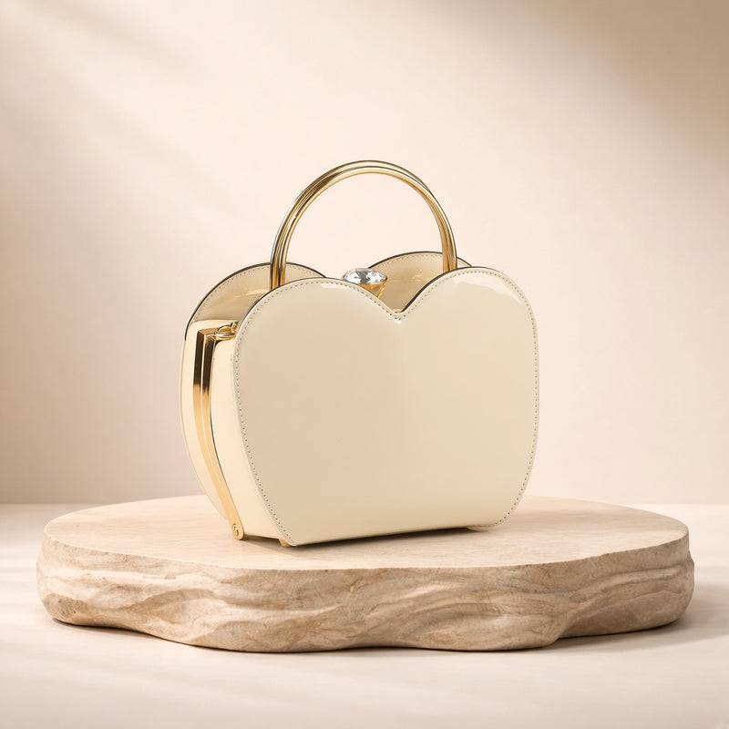 Sac coquille en cuir verni blanc cassé à fermoir bijou, posé sur un socle en pierre, vue produit