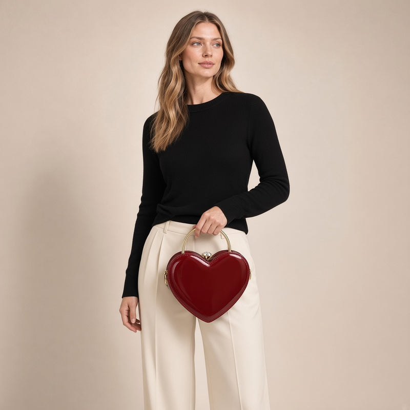 Sac coquille en cuir verni bordeaux à fermoir bijou, porté par une femme sur fond beige