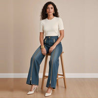 Jean large indigo à zips dorés, assise sur un tabouret – SAKIWÉ