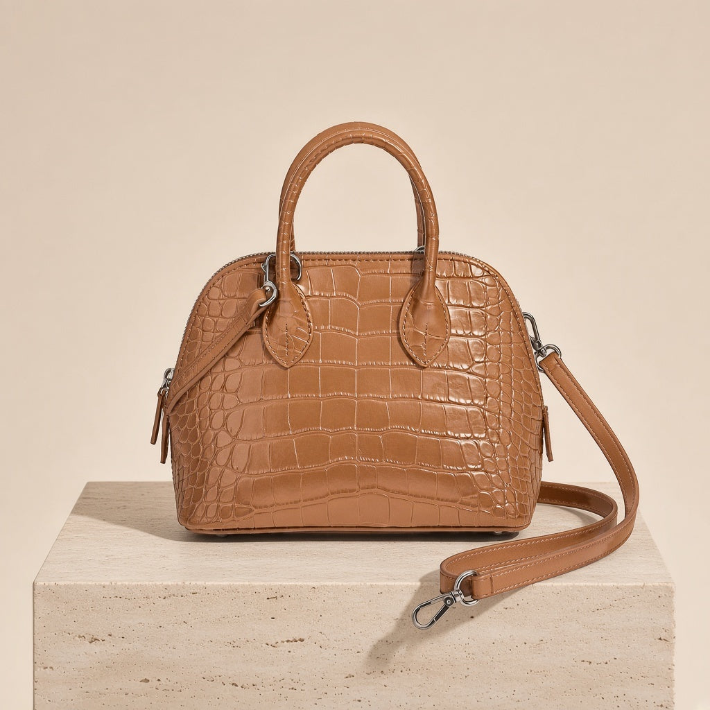 Mini sac bowling en cuir effet croco caramel posé sur un socle en pierre, bandoulière amovible