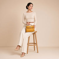 Pochette en cuir effet croco SAKIWE jaune moutarde, portée par une mannequin, assise, pochette sur les genoux