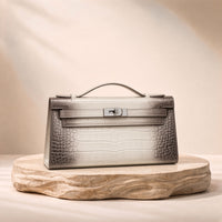 Pochette en cuir mat effet croco SAKIWE blanc nuancé, posée sur un socle en pierre