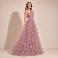 Femme de trois quarts dans la robe longue à une épaule rose poudré, main sur la jupe en tulle