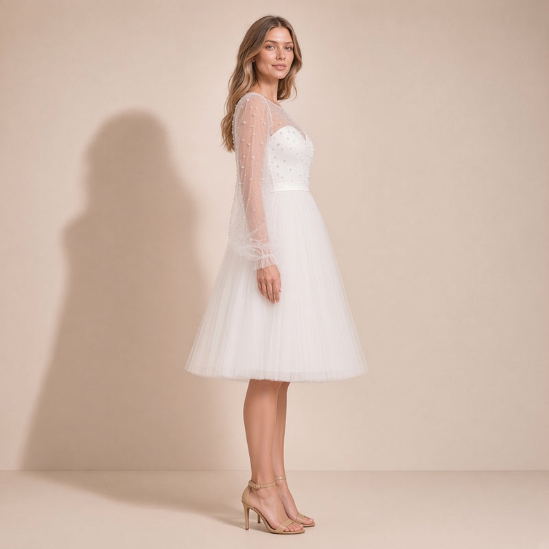 Femme de profil dans la robe de mariée courte ivoire, manches en tulle et jupe au genou