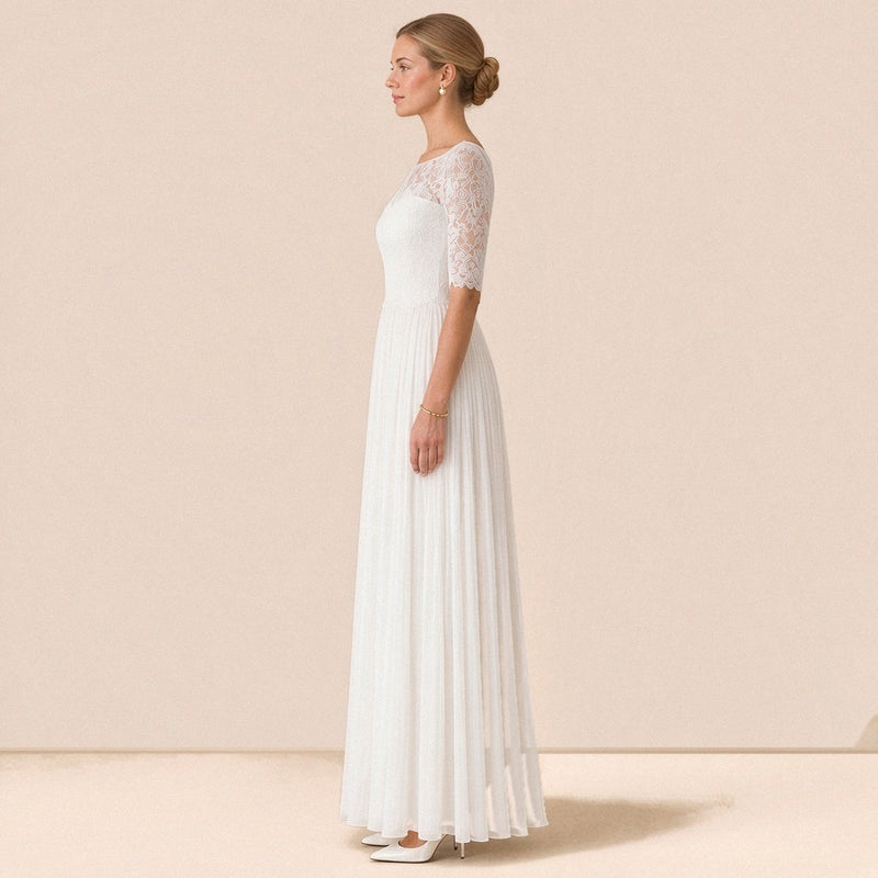 Robe de mariée en dentelle de profil, jupe plissée fluide jusqu’au sol