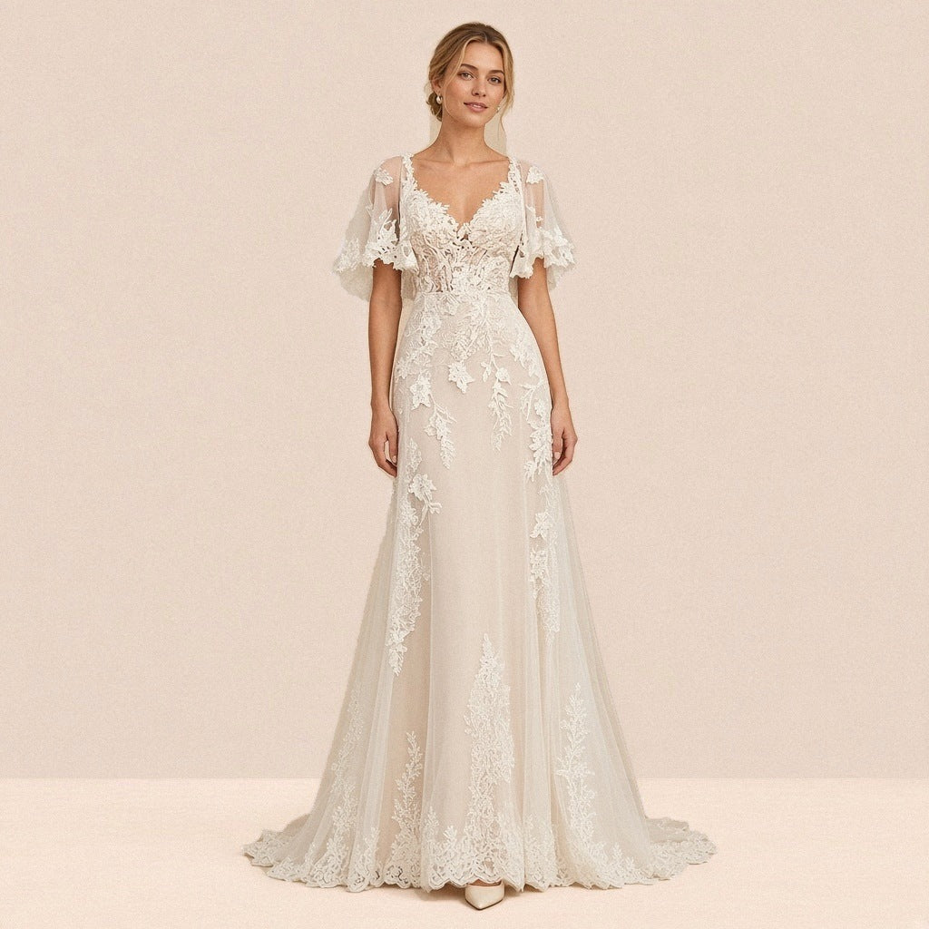 Robe de mariée longue ivoire en dentelle et tulle portée de face, décolleté en V et manches cape
