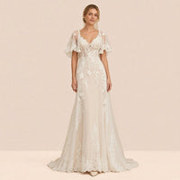 Robe de mariée longue ivoire en dentelle et tulle portée de face, décolleté en V et manches cape