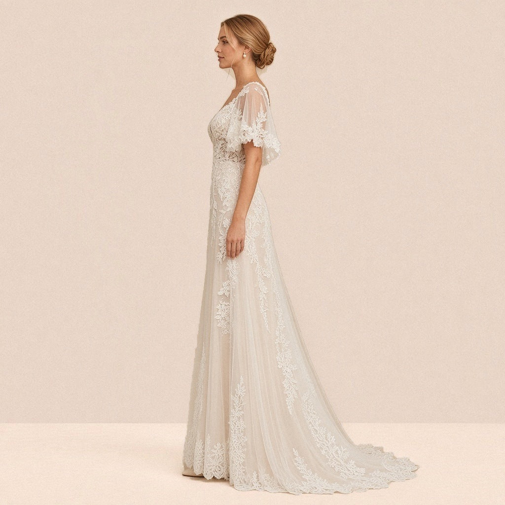 Robe de mariée en dentelle de profil, manches cape et traîne en tulle