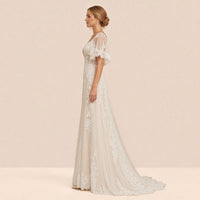 Robe de mariée en dentelle de profil, manches cape et traîne en tulle