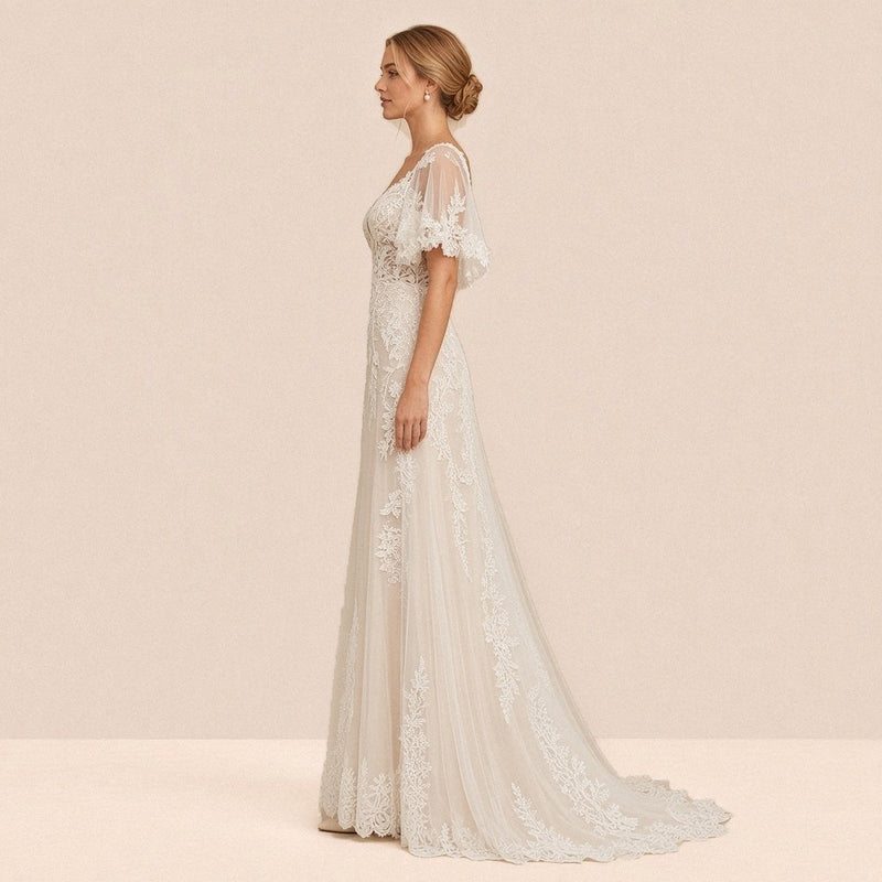 Robe de mariée en dentelle de profil, manches cape et traîne en tulle