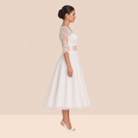 Robe de mariée en dentelle de profil, manche au coude et ceinture champagne