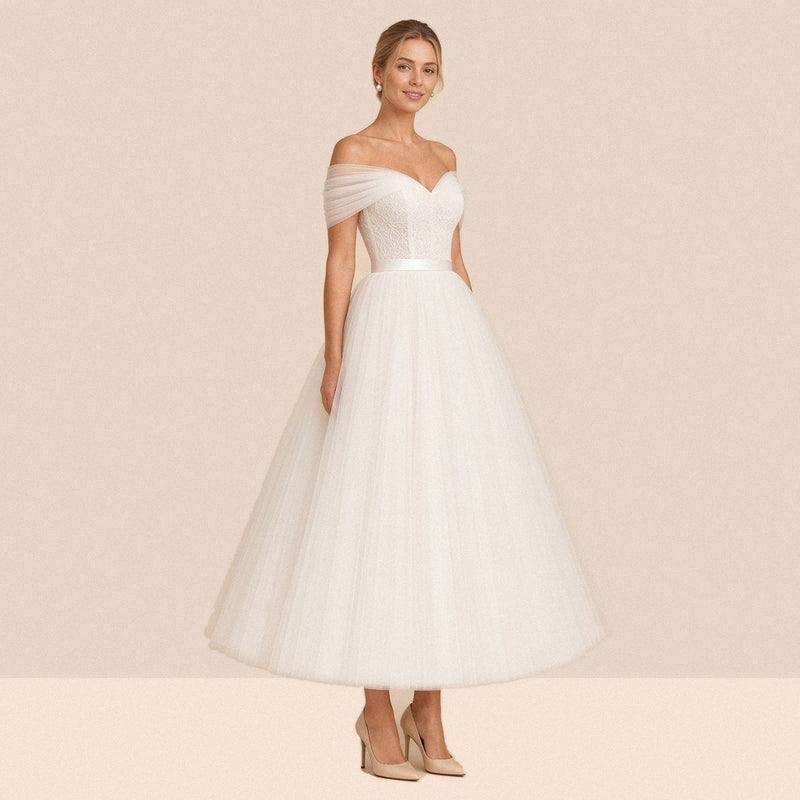 Robe de mariée ivoire mi-longue en tulle à épaules dénudées et ceinture satinée – vue de trois quarts.