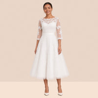 Robe de mariée blanche mi-longue en tulle portée de face, encolure illusion et manches 3/4 en dentelle