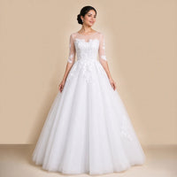 Robe de mariée princesse blanche en dentelle et tulle, col rond transparent et manches aux coudes, vue de face