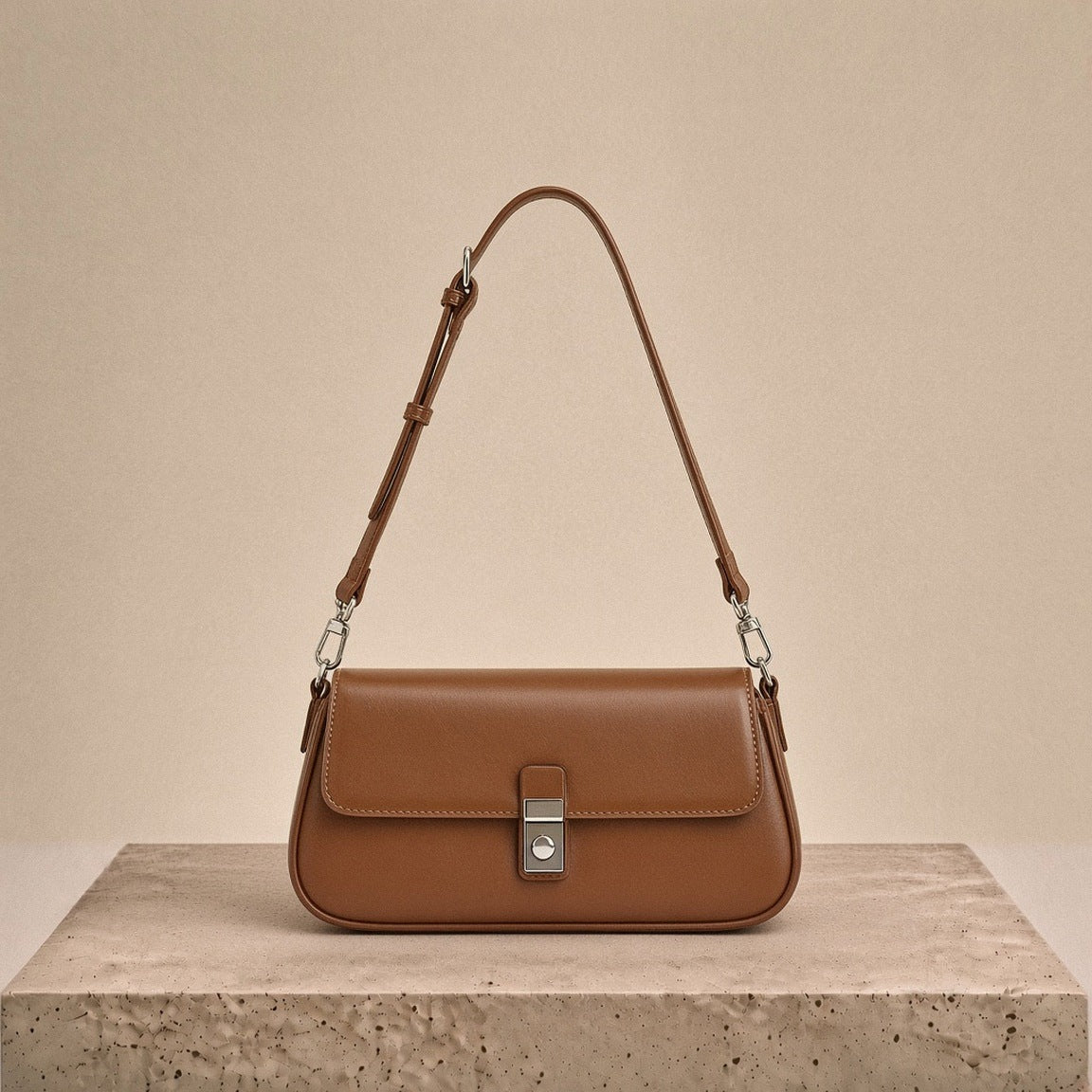 Sac baguette en similicuir caramel posé sur un socle en travertin crème