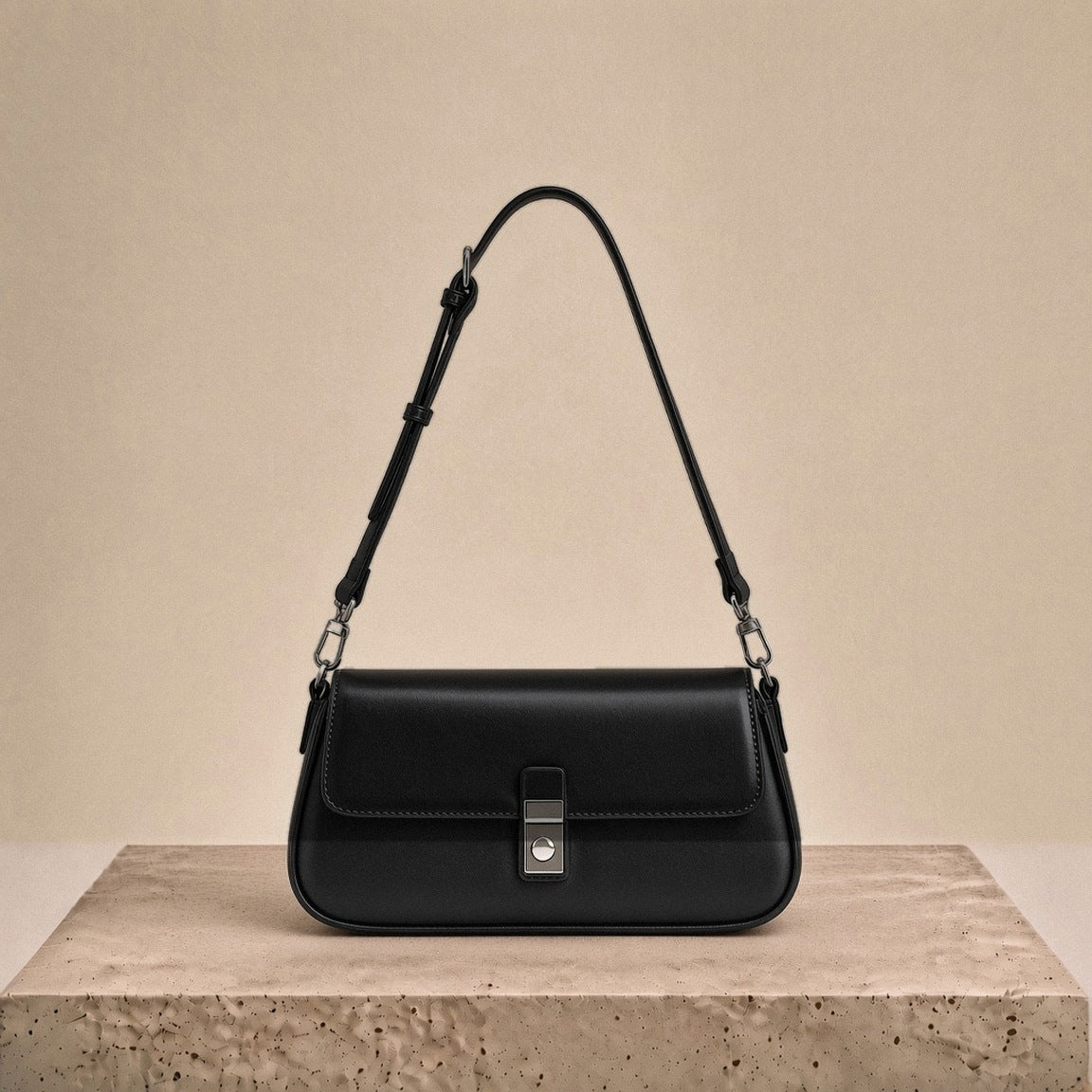 Sac baguette en similicuir noir posé sur un socle en travertin crème