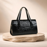 Sac Boston effet croco noir, posé sur un socle en pierre, vue produit