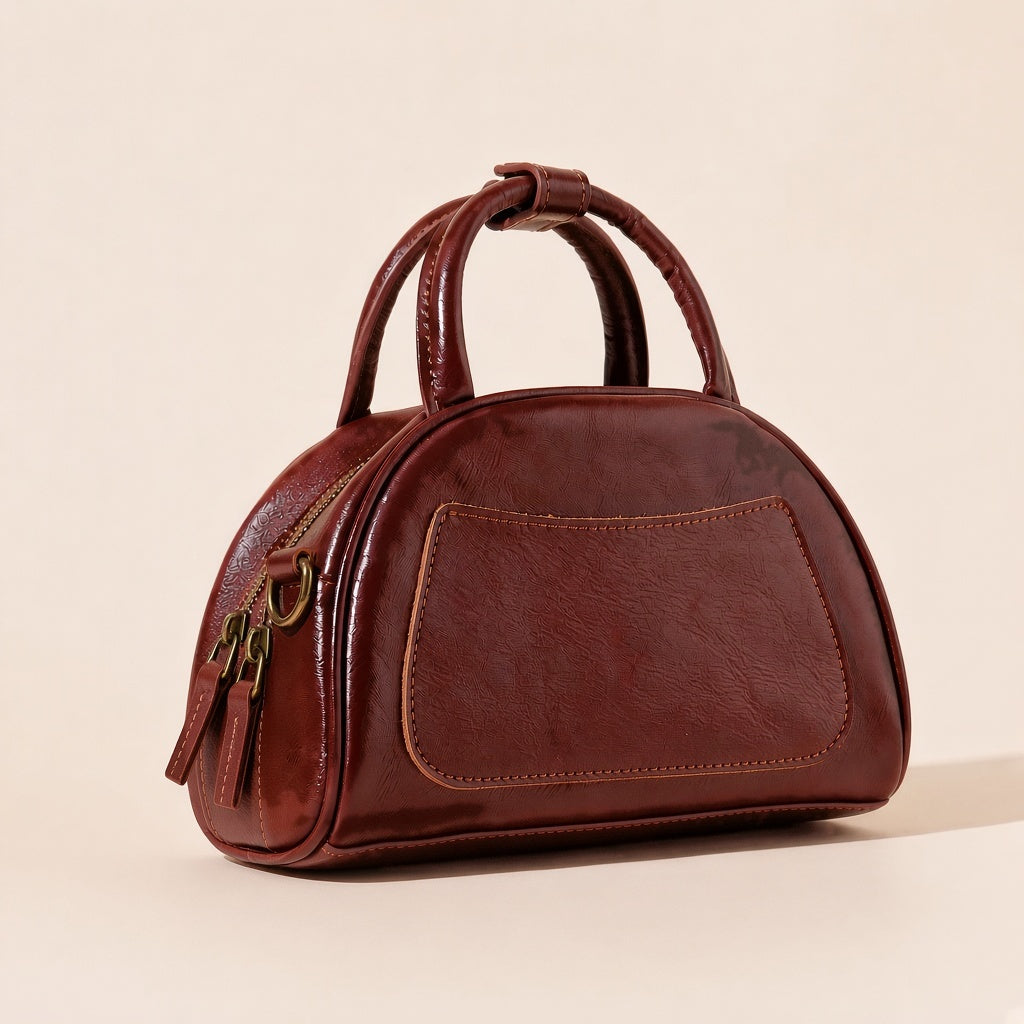 Sac bowling demi-lune en cuir ciré brun caramel vu de trois quarts, poche plaquée avant, anses roulées et tirettes de zip