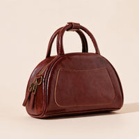Sac bowling demi-lune en cuir ciré brun caramel vu de trois quarts, poche plaquée avant, anses roulées et tirettes de zip
