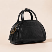 Sac bowling demi-lune en cuir ciré noir vu de trois quarts, poche plaquée avant, anses roulées et tirettes de zip