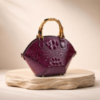 Sac coquille effet croco violet à anse bambou, posé sur un socle en pierre, vue produit
