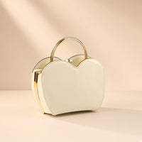 Sac coquille en cuir verni blanc cassé à fermoir bijou, vue de trois quarts sur fond beige