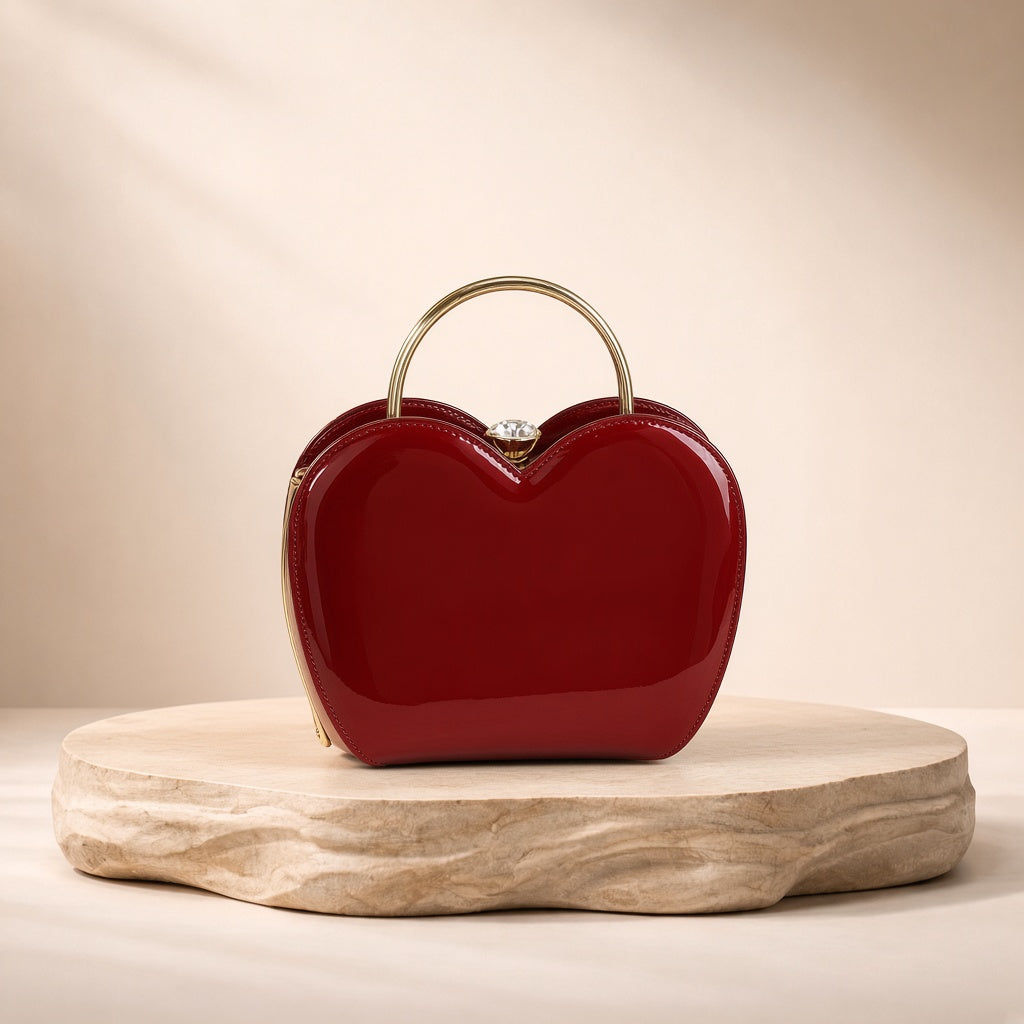 Sac coquille en cuir verni bordeaux à fermoir bijou, posé sur un socle en pierre, vue produit