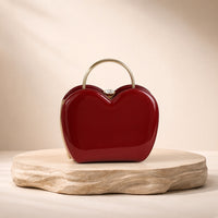 Sac coquille en cuir verni bordeaux à fermoir bijou, posé sur un socle en pierre, vue produit