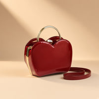Sac coquille en cuir verni bordeaux à fermoir bijou, vue de trois quarts sur fond beige