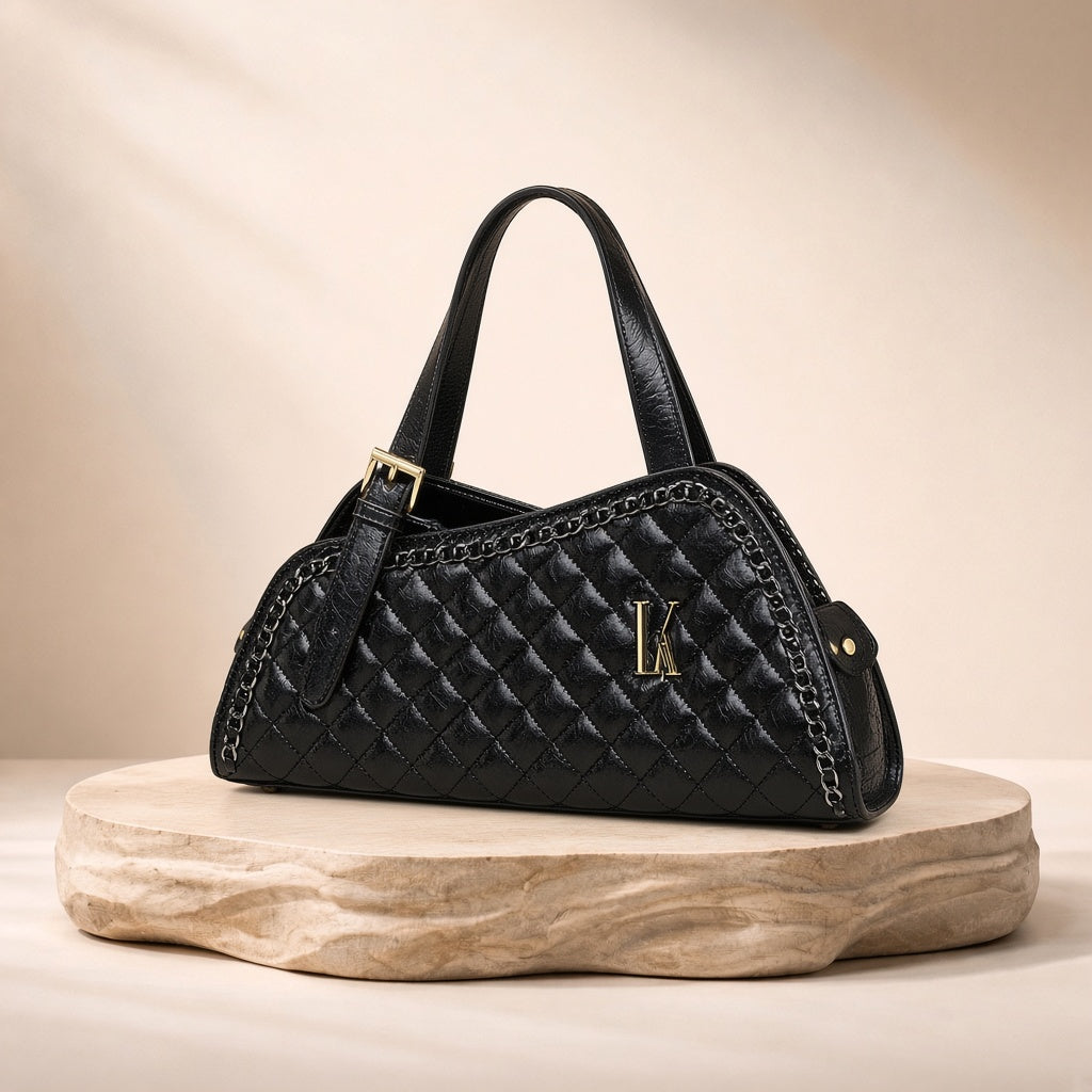 Sac porté épaule en cuir matelassé à chaîne SAKIWE noir, posé sur un socle en pierre