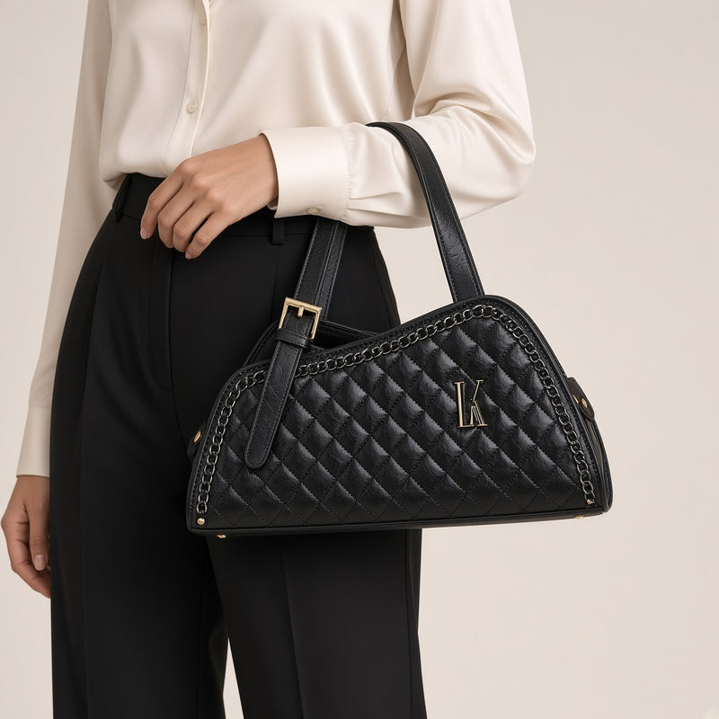 Sac porté épaule en cuir matelassé noir, détail de la boucle dorée tenu à la main