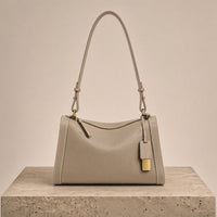 Sac porté épaule oreiller en cuir grainé taupe, posé sur un socle en pierre