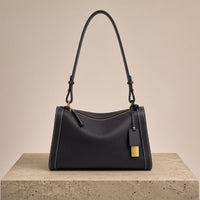 Sac porté épaule oreiller en cuir grainé graphite, posé sur un socle en pierre
