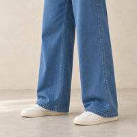 Détail des jambes larges du pantalon en jean bleu et des chaussures portées avec l’ensemble.