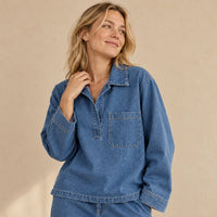 Détail du haut en jean bleu : col chemise, patte de boutonnage courte et poche poitrine.
