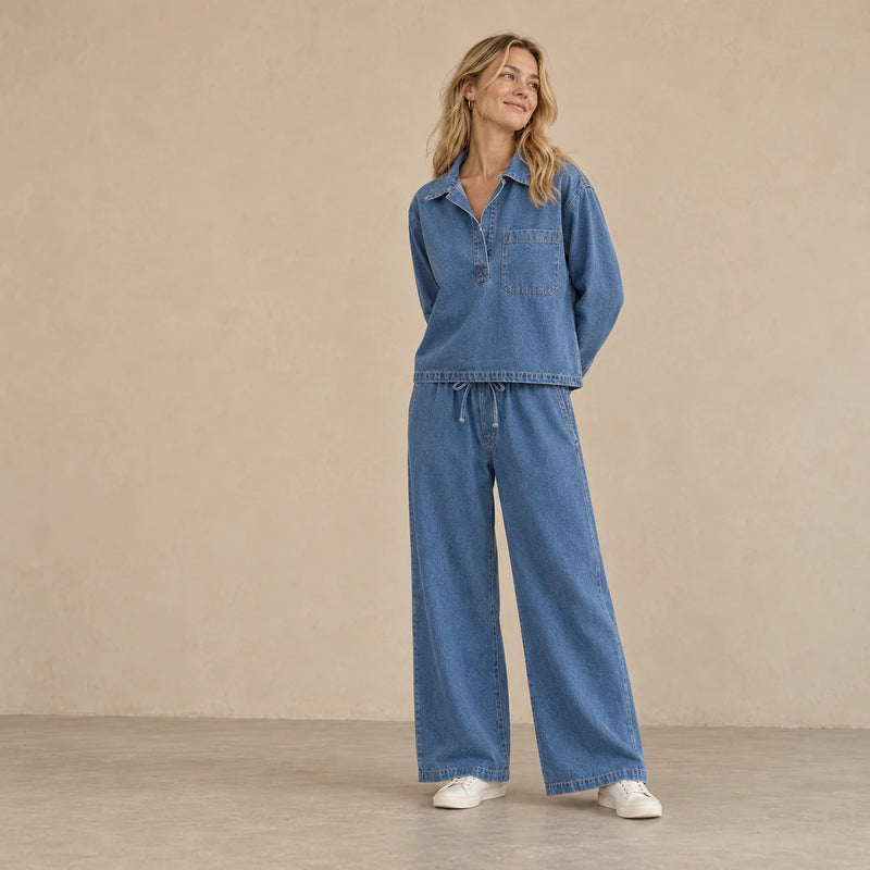 Ensemble en jean bleu à haut à col et pantalon large, porté en pose trois quarts dans un intérieur beige clair.