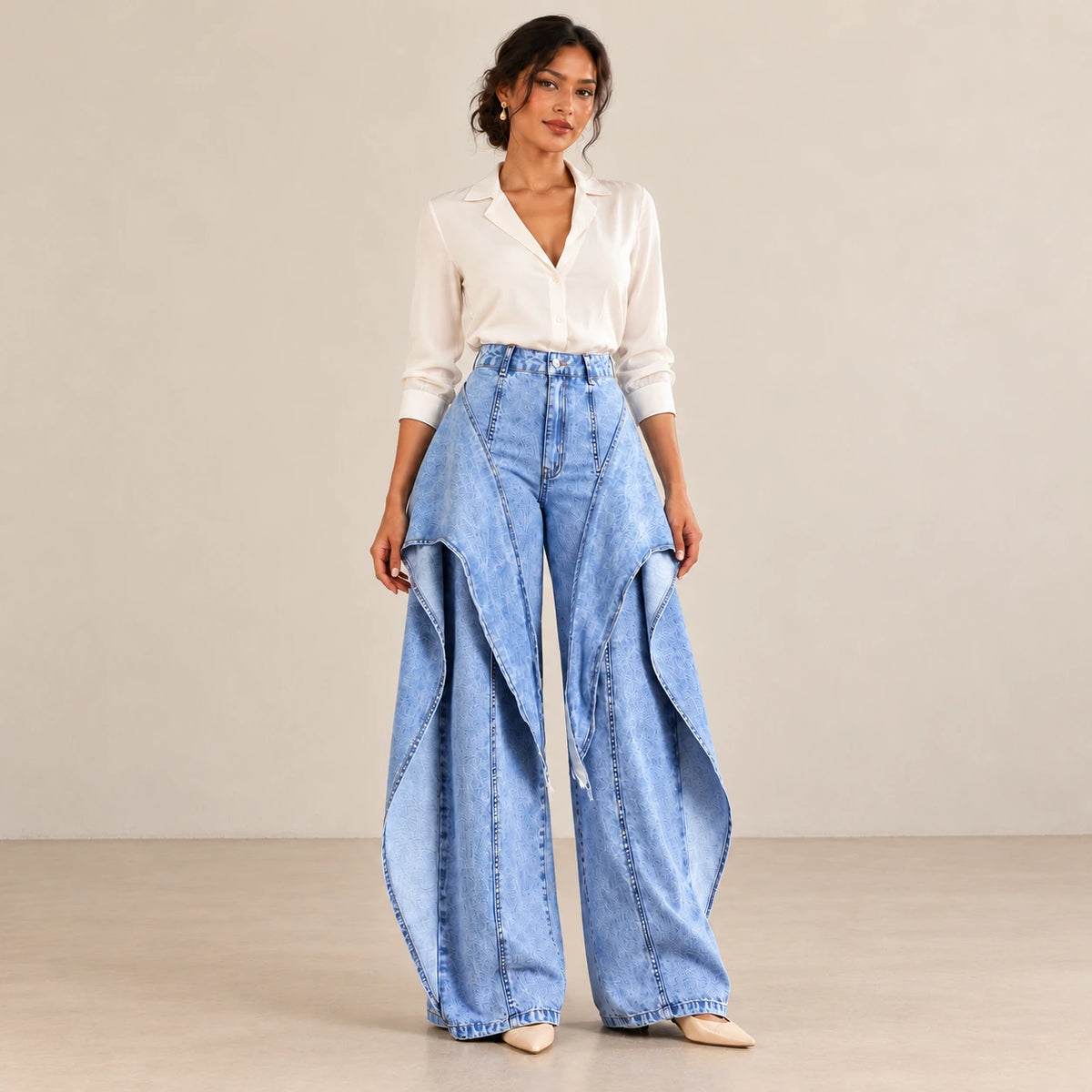 Jean large bleu à panneaux superposés porté de face avec une blouse ivoire.