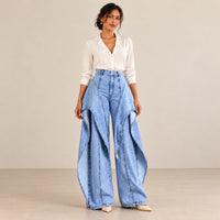 Jean large bleu à panneaux superposés porté de face avec une blouse ivoire.