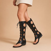 Sandales montantes noires ajourées à lacets portées, vue des jambes sur fond beige