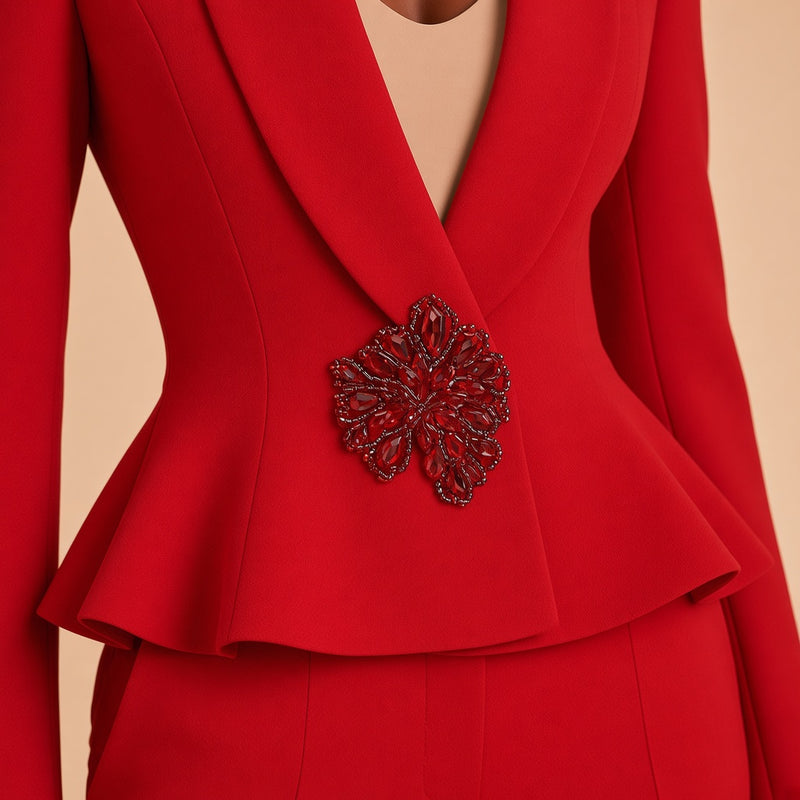 Gros plan sur le col châle, la basque et la broche bijou perlée du blazer rouge