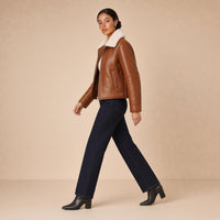 Veste courte ouatinée en cuir de mouton à col peluche SAKIWE caramel brûlé, portée en marchant de profil
