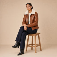 Veste courte ouatinée en cuir de mouton à col peluche SAKIWE caramel brûlé, portée assise sur un tabouret